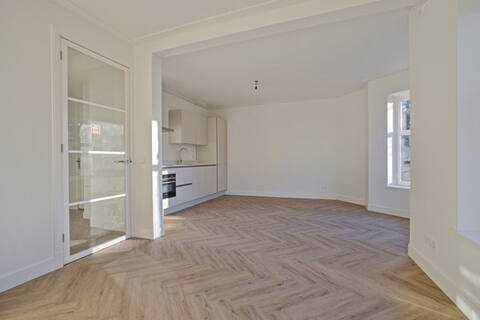 Moderne keuken met witte kasten en houten vloer in een lichte woonkamer.